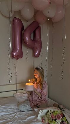 a woman sitting on her bed holding a plate with a candle in front of balloons