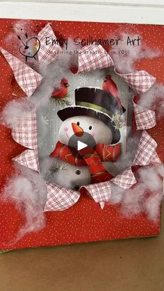 a red box with a snowman in the center and two birds on it's side