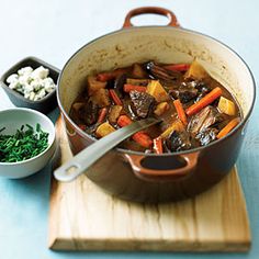 a pot filled with stew and vegetables next to a bowl of cottage cheese on a cutting board