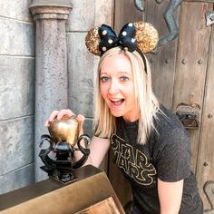 a woman is posing with her mickey mouse ears on and holding up a golden vase