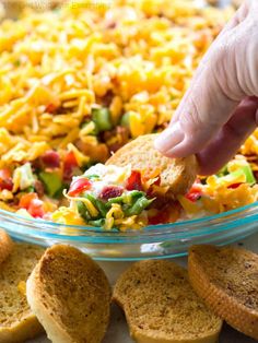 a hand dipping a cracker into a bowl of mexican salad