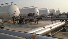 several large white tanks sitting next to each other on top of a cement ground with metal pipes