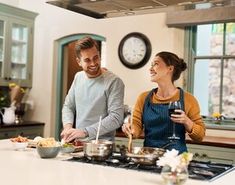 a man and woman standing in a kitchen with food on the counter top, smiling at each other