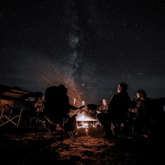 three people sitting around a campfire at night with the stars in the sky above