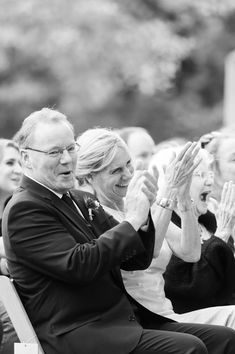 an older couple sitting on a bench and clapping at the same time as others look on