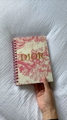 a hand holding a pink notebook with the word dior on it