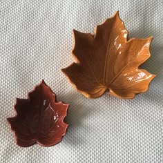 two brown and orange leaf shaped dishes sitting on top of a white cloth covered table