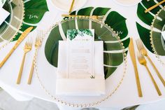 a place setting with plates, napkins and gold cutlery on a white table cloth