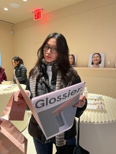 a woman holding a sign that says glossier