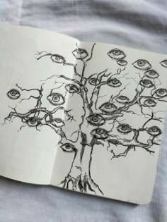 an open book with drawings of trees and eyeballs on the pages, sitting on a bed sheet