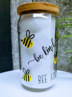 a jar with bees painted on it sitting on a table next to a potted plant