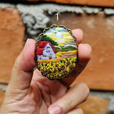 a hand holding a beaded brooch in front of a brick wall