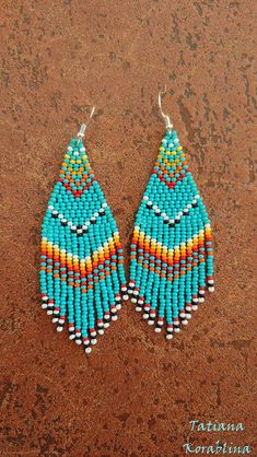 a pair of blue and yellow beaded earrings sitting on top of a dirt ground