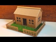 a paper model of a small house with grass growing in the yard and fence around it