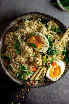 a bowl filled with noodles, meat and vegetables next to chopsticks on a table