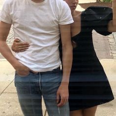 a man and woman standing next to each other on a sidewalk with trees in the background