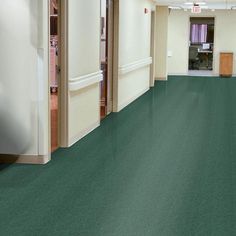 an empty room with green flooring and white walls in the center is a door leading to another room