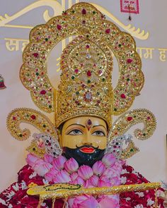 the statue is adorned with gold and pink flowers in front of a white wall behind it