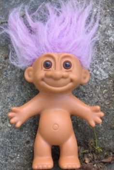 a troll doll with purple hair standing next to a rock