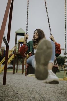 a woman sitting on top of a swing next to a child's play ground