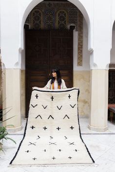 a woman sitting on the ground holding up a white and black blanket in front of a doorway