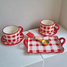 two red and white checkered dishes with spoons on them sitting on a counter