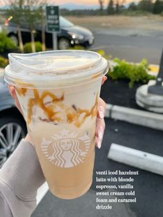 a person holding up a starbucks drink in front of a parking lot