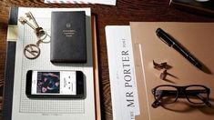 an assortment of office supplies on top of a wooden table next to a pen and eyeglasses