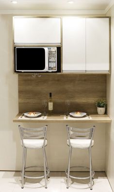 two white chairs sitting in front of a counter with plates on it and a microwave above them