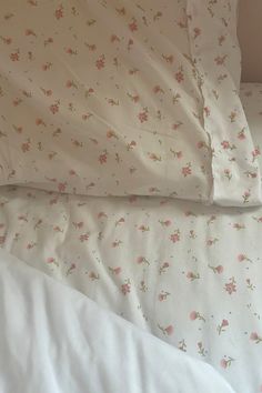 a bed with white sheets and pink flowers on it's side, next to a pillow case