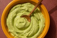 a yellow bowl filled with green guacamole on top of a pink surface