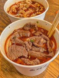 two bowls of beef soup with chopsticks in them on a wooden table top