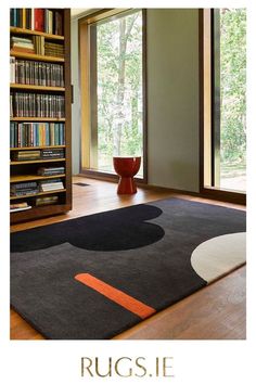 the rug is in front of a book shelf with books on it and an orange vase next to it