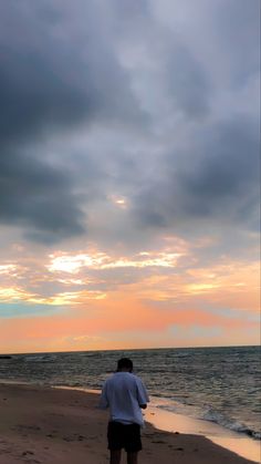 a man standing on top of a beach next to the ocean under a cloudy sky