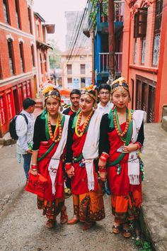 group of young people dressed in traditional clothing standing on the side of a road next to red brick buildings