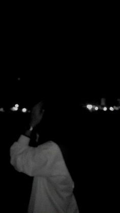 a person standing in the dark with their hand up to his face and looking into the distance