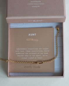 an open pink box with a gold chain attached to it and a card on the inside