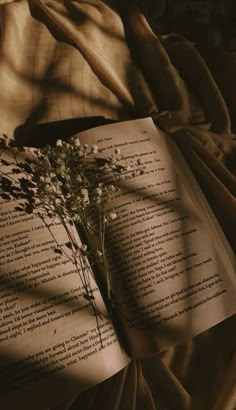 an open book sitting on top of a bed next to a bouquet of wildflowers