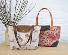 two purses sitting on top of a table next to each other with flowers in the background