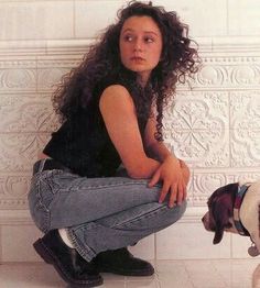 a woman sitting on the floor next to a small dog and looking up at her