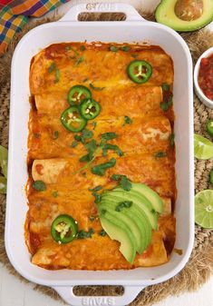 an enchilada casserole in a white dish with avocado slices on the side