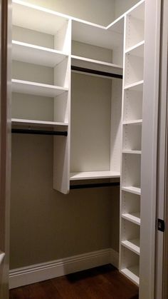 an empty walk in closet with white shelving and wood flooring on the side