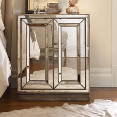 a mirrored cabinet sitting on top of a wooden floor next to a white rug and lamp