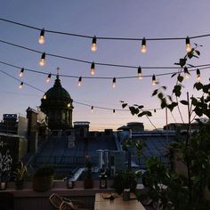 some lights are hanging over a table and chairs on top of a roof in the evening