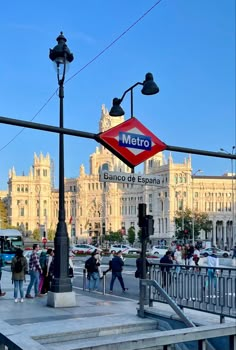 people are walking on the sidewalk in front of a metro station and some large buildings