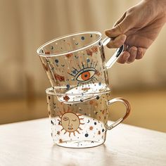 a person is holding a spoon over two cups with drawings on the inside and outside