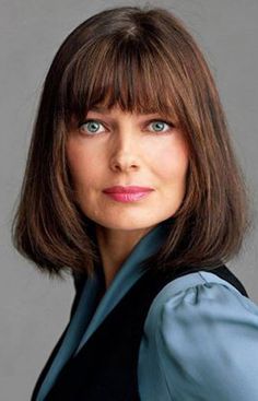 a woman with brown hair and blue eyes posing for a photo in front of a gray background