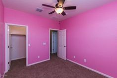 an empty room with pink walls and ceiling fan in the center, carpeted floor