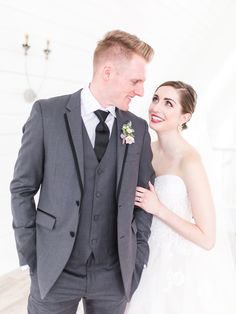 a bride and groom standing next to each other in front of a white wall smiling