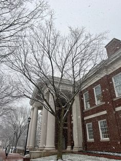 an old brick building with columns and trees in the snow on a college campus during winter